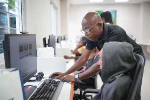Kwesi Dyer, ICT Technical Officer for the La Brea ICT Access Centre showing a young community member how to use their computer.